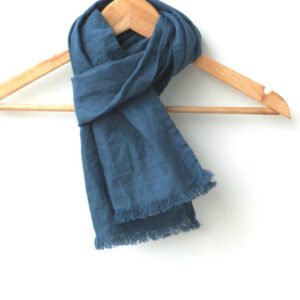 Small denim blue handmade linen scarf with frayed edges hanging on a wooden hanger against a white background.