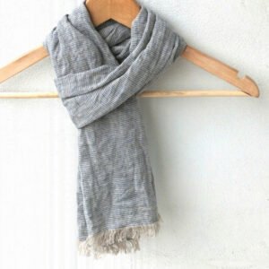 Knotted blue and grey horizontal striped linen scarf on a wooden hanger, highlighting the robust fabric and frayed edges.