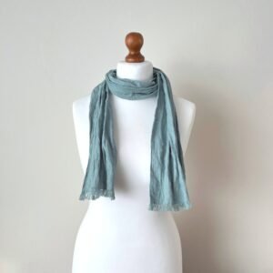 Ice blue green linen scarf tied around a white mannequin neck, showing a fabric drape and small fringe edges.